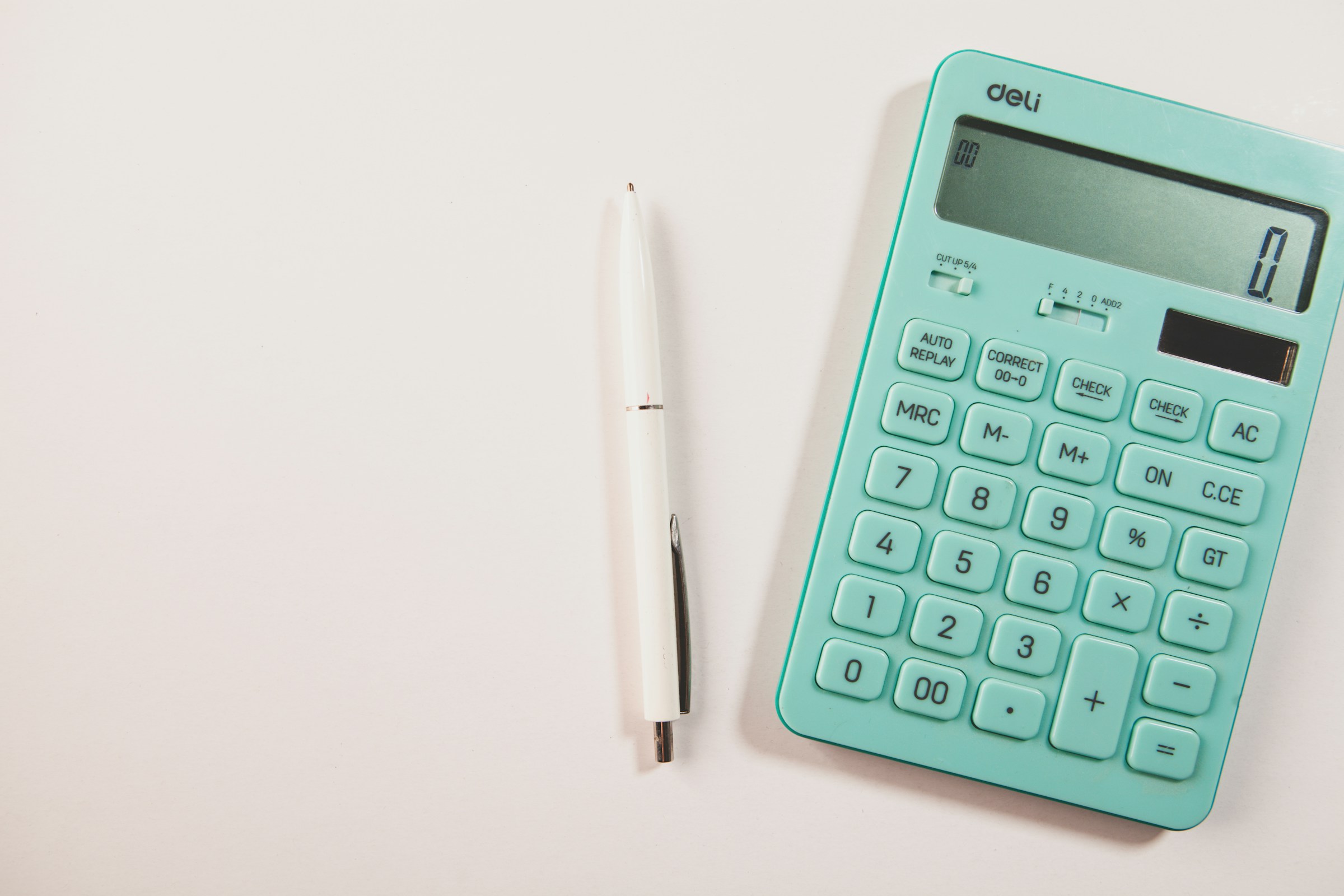 A teal calculator and white pen on a white surface, with clear space on the left.